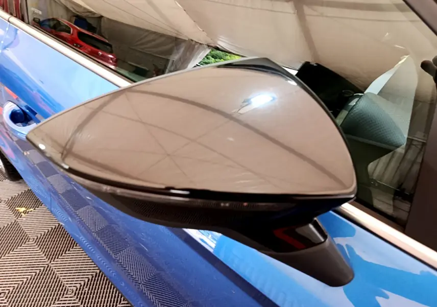 Rétroviseur droit noir brillant sur porte bleue d'une SEAT Arona 2022 vue en gros plan intérieur garage.