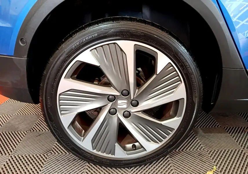Gros plan sur la roue avant droite d'une SEAT Arona bleue, mettant en valeur la jante aluminium au design moderne.