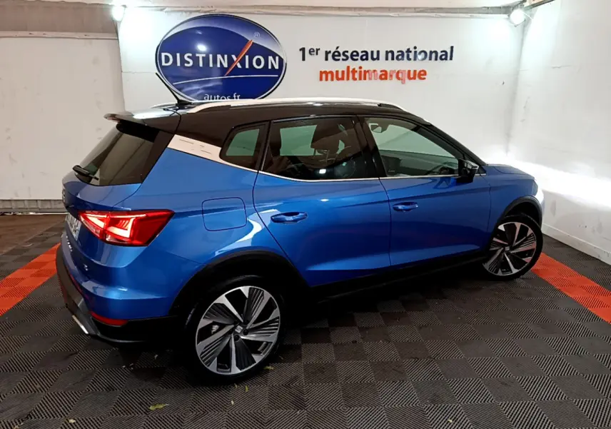 SEAT Arona bleu en vue 3/4 arrière droit, toit noir contrasté et jantes alliage distinctives dans un showroom