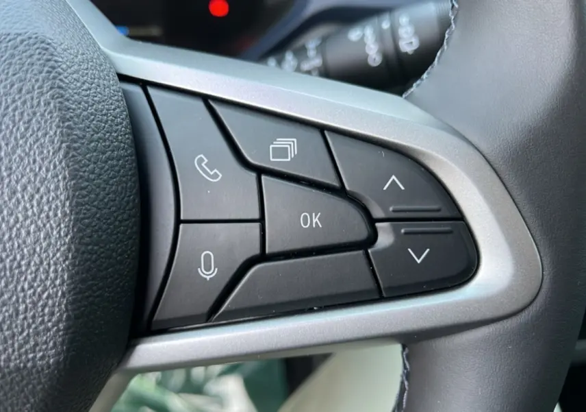 Gros plan sur les commandes multifonctions noires du volant cuir du Dacia Bigster Hybrid 155 Expression Plus, intérieur gris.