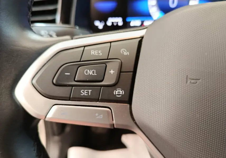 Gros plan sur le volant multifonctions en cuir et alu de la Volkswagen Polo gris clair 2023, avec commandes de régulateur.