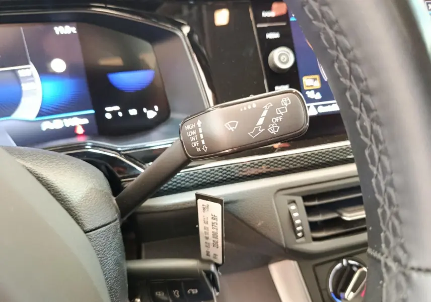 Gros plan sur la manette d’essuie-glace à gauche du volant cuir d’une Volkswagen Polo gris clair, tableau de bord numérique en arrière-plan.