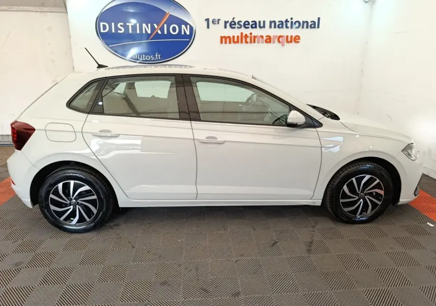 Vue latérale droite d'une Volkswagen Polo gris clair 2023 avec jantes alliage noires et blanches, en intérieur showroom.