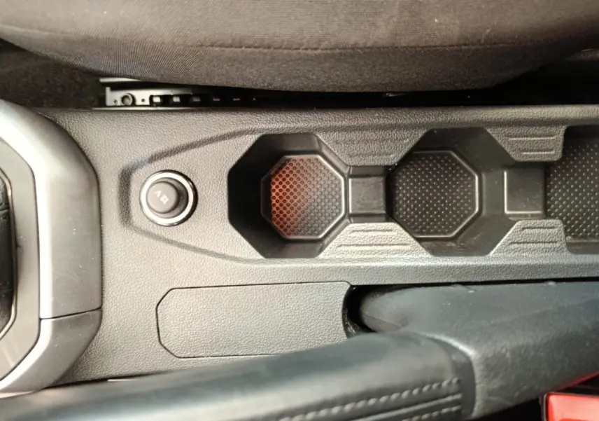 Gros plan sur la console centrale noire de la Volkswagen Polo 2023, montrant le bouton 12V et le frein à main cuir.