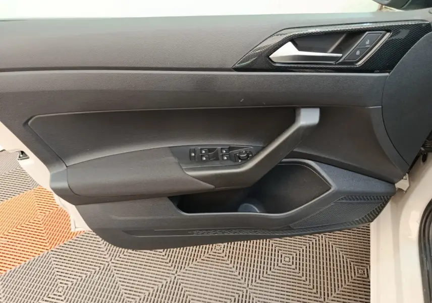 Vue latérale du panneau de porte avant gauche noir d'une Volkswagen Polo 2023, avec commandes électriques et poignée intégrée.