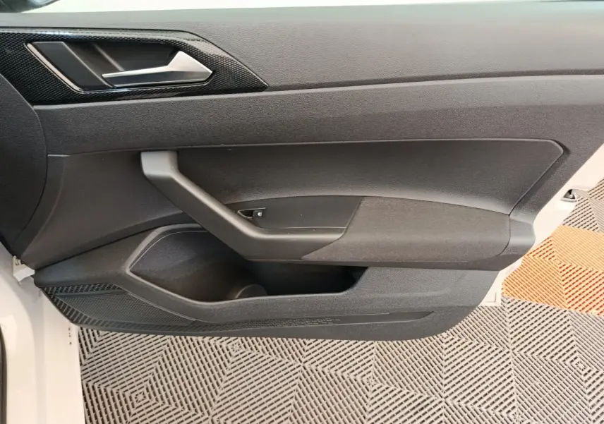 Vue latérale du panneau de porte intérieur gris foncé de la Volkswagen Polo 2023, avec poignée intégrée et rangement.