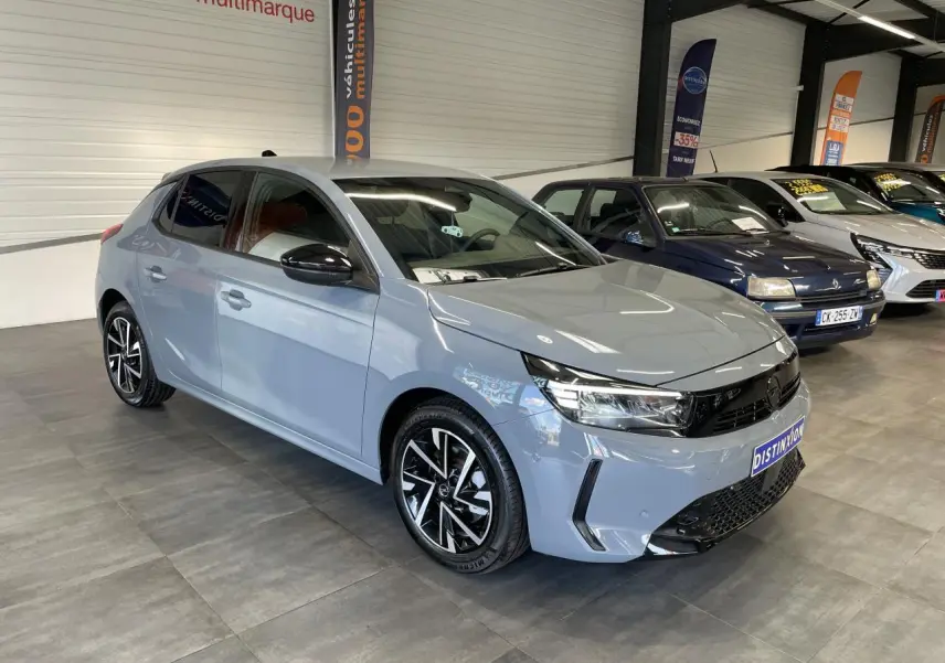 Vue 3/4 avant d'une Opel Corsa gris clair avec jantes alliage noires et vitres arrière surteintées en showroom.