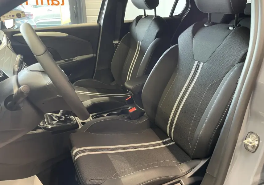 Intérieur avant droit d’Opel Corsa gris, sièges sport noirs avec bandes blanches et volant cuir synthétique.