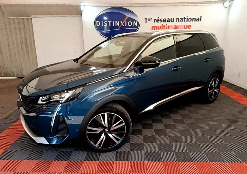 Peugeot 5008 bleu en 3/4 avant droit, jantes alliage noires et chrome, stationné en intérieur showroom