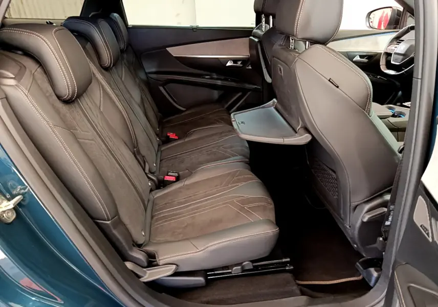 Vue côté gauche de l'intérieur arrière du Peugeot 5008 bleu, sièges en cuir marron avec tablette rabattable intégrée.