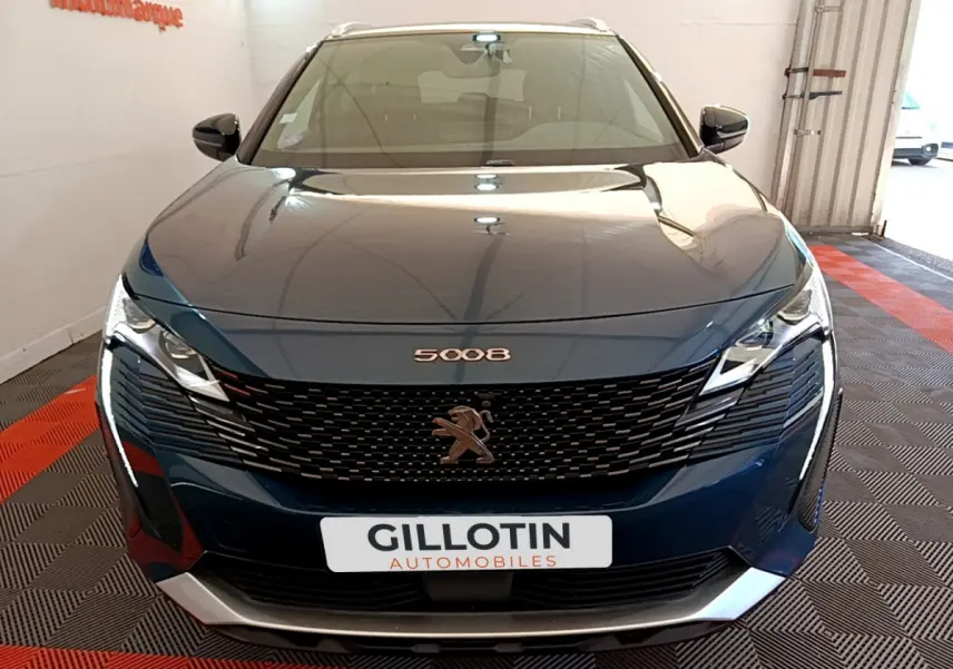 Vue frontale d'un Peugeot 5008 bleu avec calandre noire et logo lion, dans un showroom éclairé.