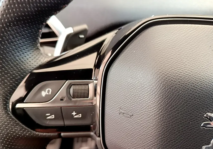 Gros plan sur les commandes gauche du volant cuir noir du Peugeot 5008 bleu, avec logo lion visible.