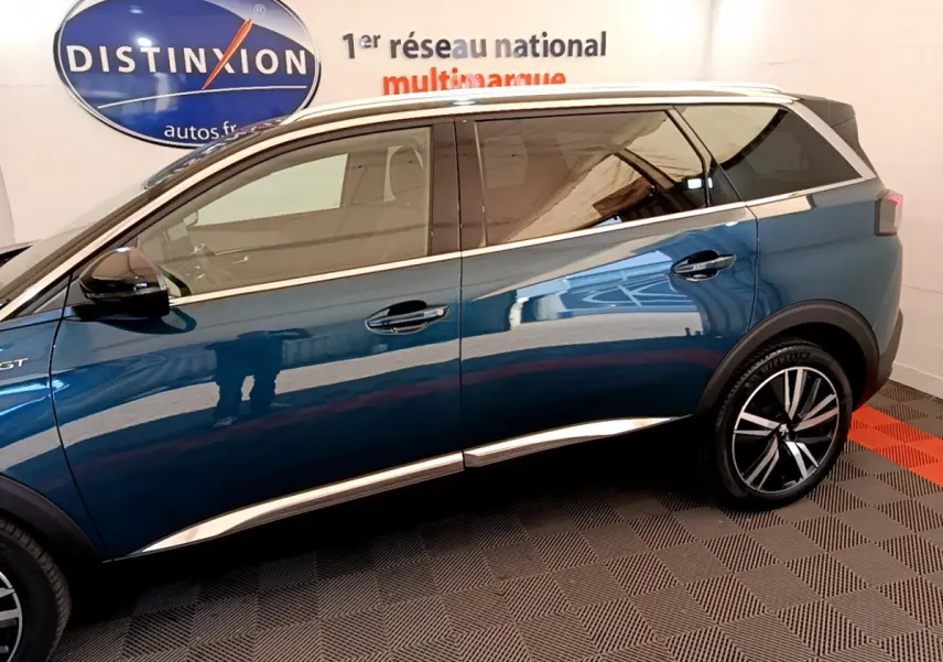 Profil côté gauche du Peugeot 5008 bleu 2021 GT Pack avec jantes alliage et vitres teintées en intérieur showroom.