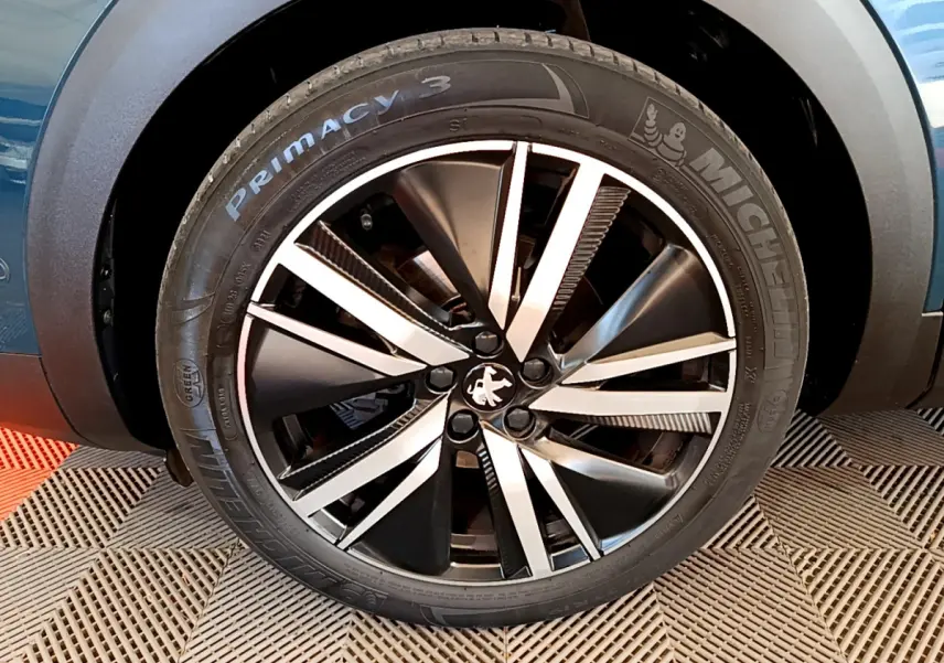 Gros plan sur la roue avant droite bleu d'un Peugeot 5008 GT Pack avec jante alliage bicolore distinctive.