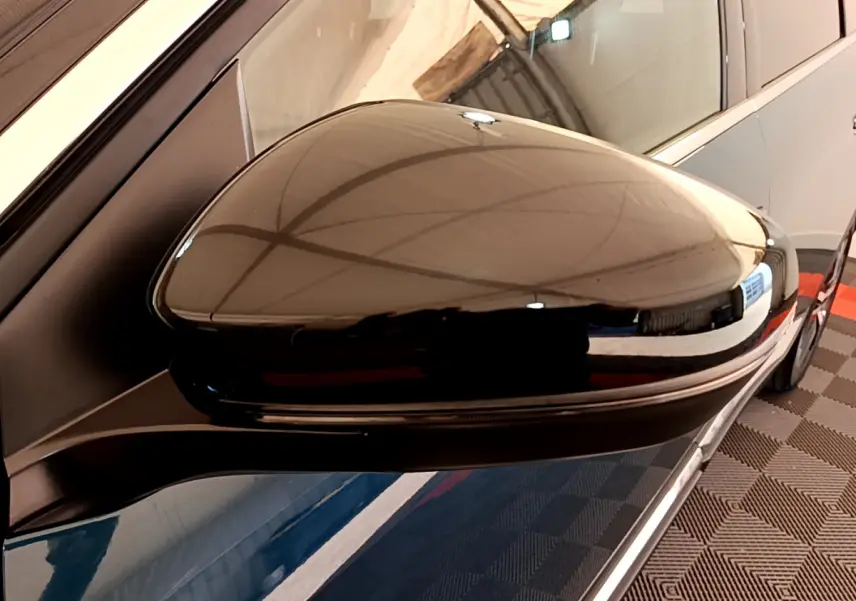 Rétroviseur côté gauche noir brillant du Peugeot 5008 bleu, vue rapprochée avec reflet de l'environnement intérieur.