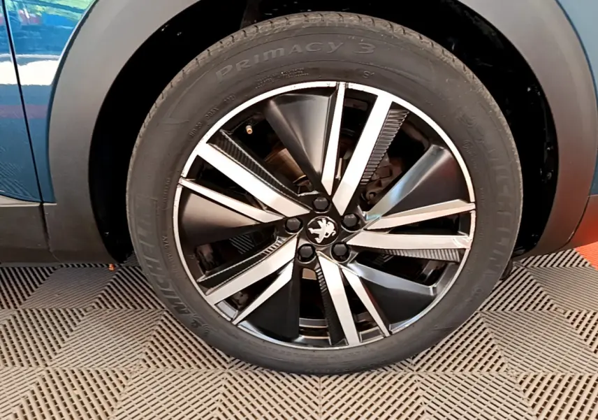 Gros plan sur la roue avant droite du Peugeot 5008 bleu, mettant en valeur la jante alliage au design moderne.