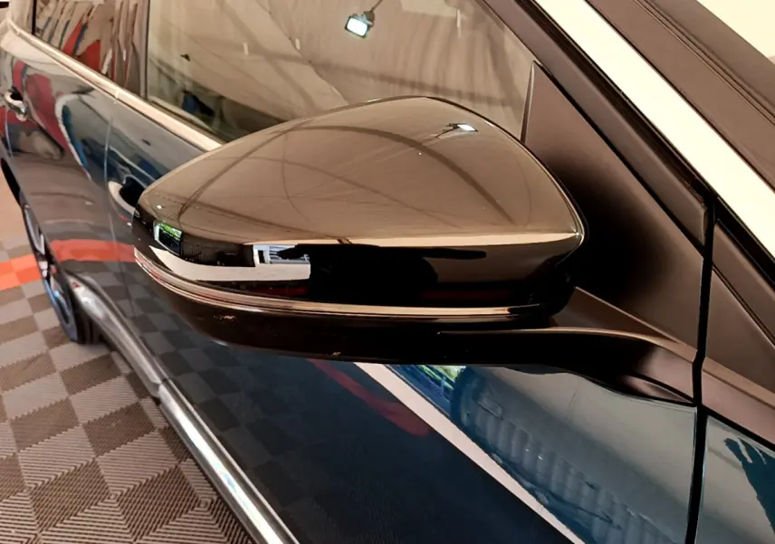 Rétroviseur côté gauche noir brillant du Peugeot 5008 bleu, avec carrosserie et poignée de porte visibles en arrière-plan.