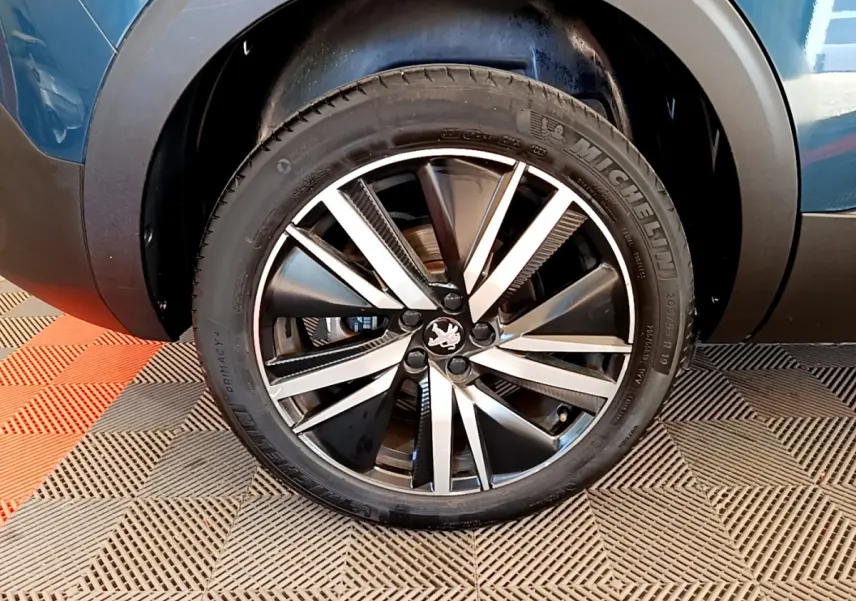 Gros plan sur la roue avant droite du Peugeot 5008 bleu, mettant en valeur la jante alliage bicolore et le pneu Michelin.