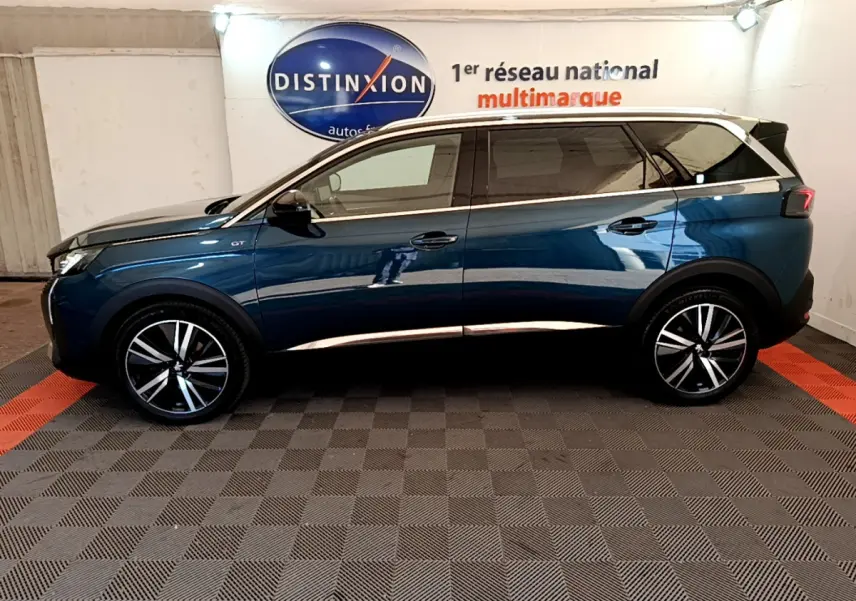 Profil côté gauche d'un Peugeot 5008 GT Pack bleu avec toit blanc et jantes alliage stylées en intérieur showroom.
