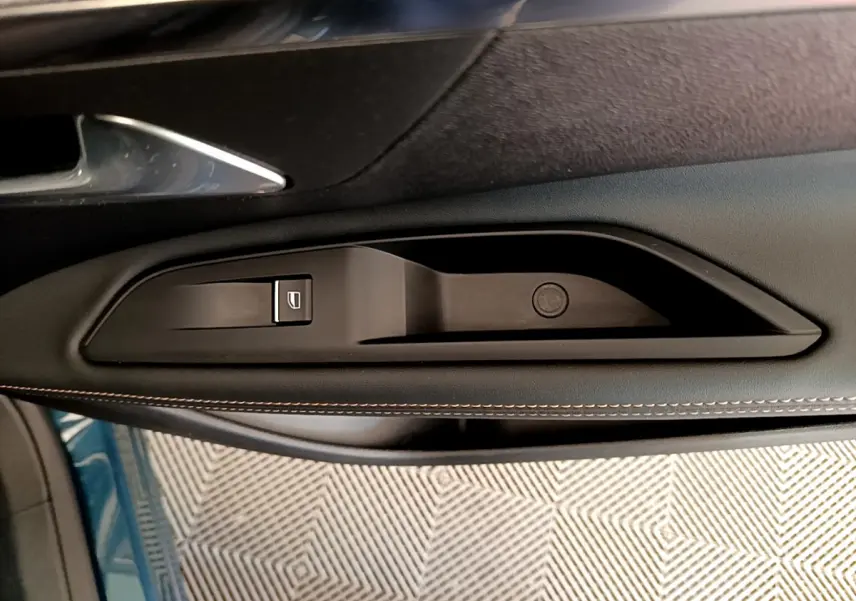 Poignée intérieure côté gauche de la porte d’un Peugeot 5008 bleu, avec bouton de commande de vitre électrique.