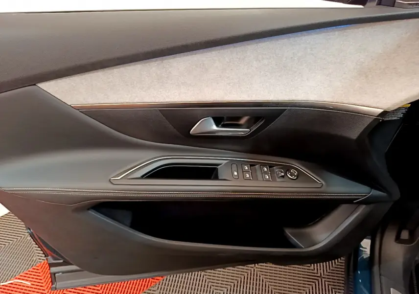 Gros plan sur la porte côté gauche du Peugeot 5008 bleu, montrant les commandes des vitres et la poignée intérieure.