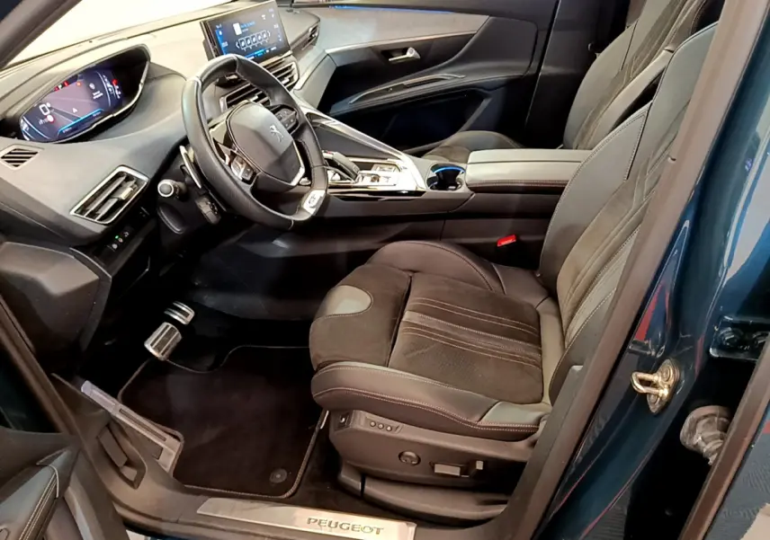 Vue intérieure côté conducteur du Peugeot 5008 bleu, mettant en valeur le tableau de bord digital et les sièges en cuir noir.