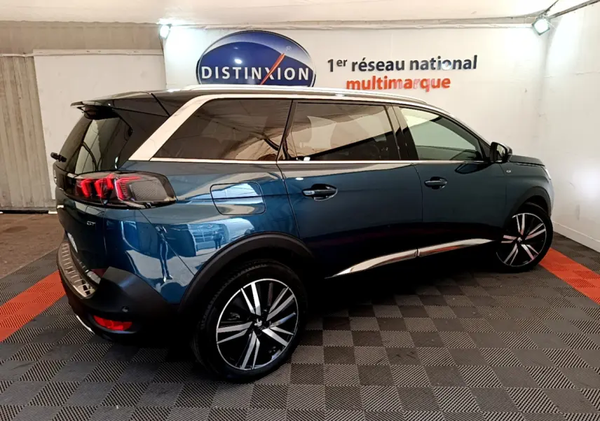 Peugeot 5008 bleu en 3/4 arrière droit, avec toit blanc et jantes alliage distinctives, en intérieur showroom.