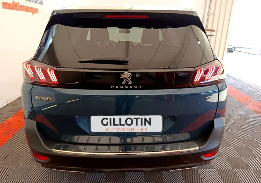 Vue arrière d'un Peugeot 5008 bleu avec feux LED en forme de griffes et logo lion central sur hayon noir brillant.