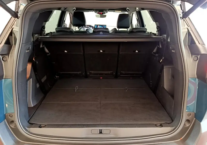 Coffre ouvert vu de l'arrière d'un Peugeot 5008 bleu 2021, sièges rabattus offrant un plancher plat spacieux.