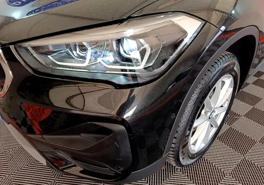 Gros plan sur le phare avant gauche et la roue d’une BMW X1 noire, mettant en valeur les détails modernes du design.