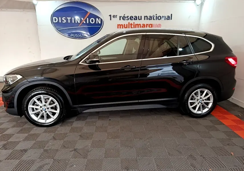 Profil côté gauche d'un BMW X1 noir 2020, finition Business Design, sur sol damier en intérieur showroom.