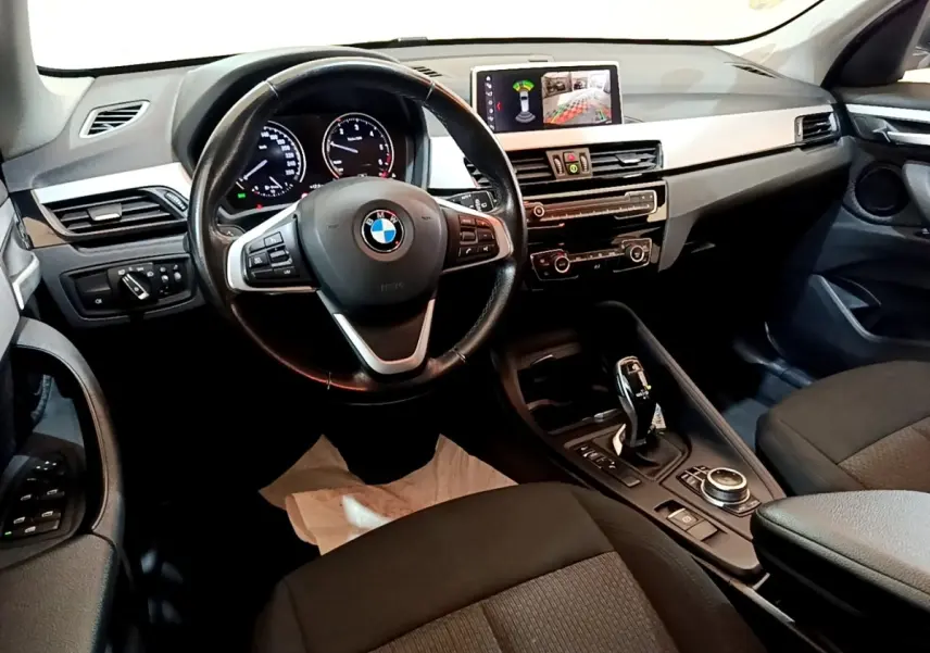 Intérieur noir de BMW X1 2020 vu côté conducteur, volant cuir multifonctions et écran tactile 8,8 pouces affichant caméra de recul.
