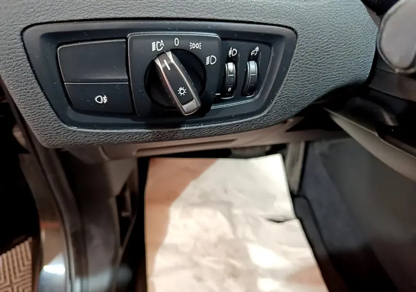 Gros plan sur les commandes d'éclairage côté gauche du tableau de bord noir du BMW X1 sDrive16d Business Design 2020.