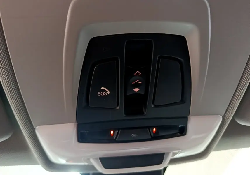 Panneau de commandes au plafond avec bouton SOS et éclairage intérieur activé dans une BMW X1 noire de 2020.