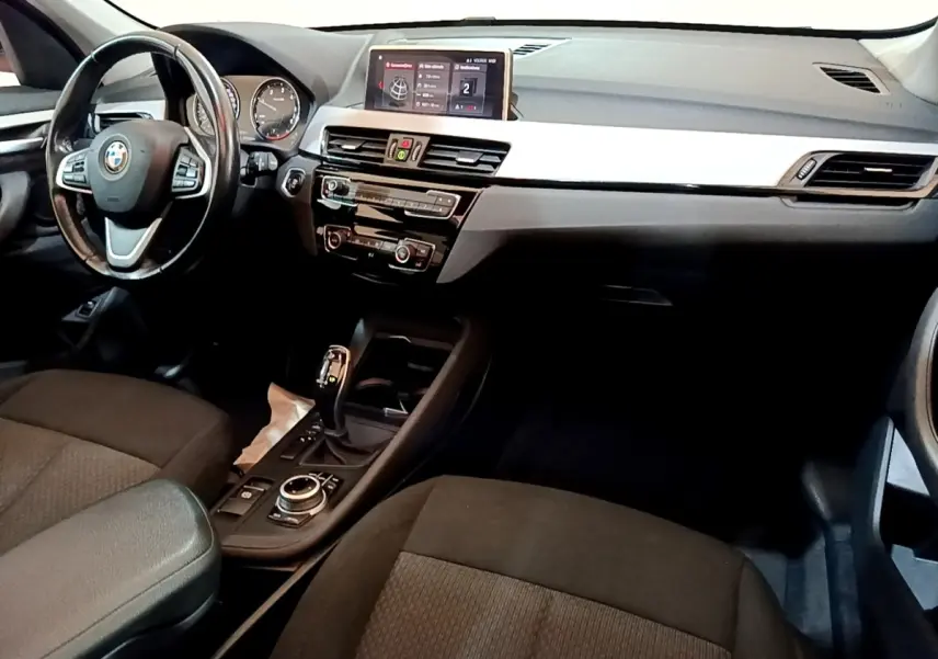 Intérieur BMW X1 sDrive16d 2020 vu côté conducteur, tableau de bord noir avec écran tactile 8,8 pouces et volant cuir.