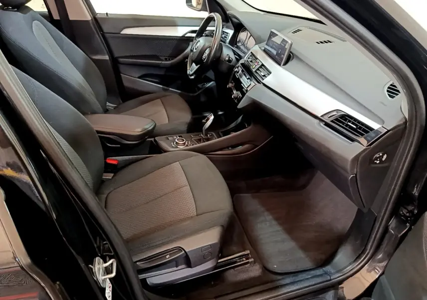 Intérieur avant droit d'une BMW X1 noire 2020, sièges tissu gris, tableau de bord avec écran tactile et console centrale.
