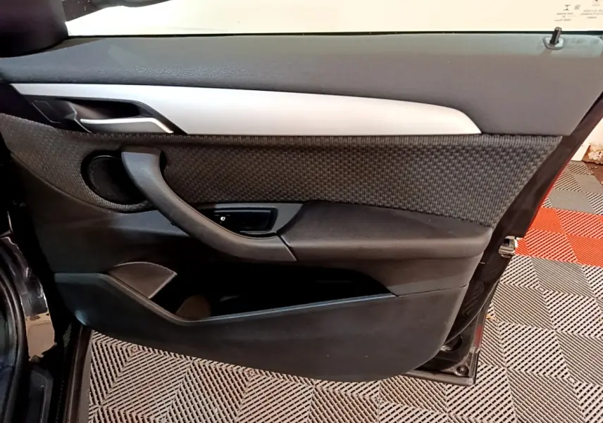 Porte intérieure côté gauche de BMW X1 noir 2020, avec habillage tissu et plastique noir, poignée intégrée et haut-parleur rond.
