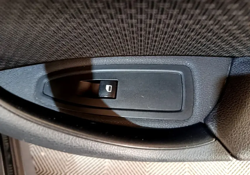 Gros plan sur le bouton de commande de lève-vitre côté conducteur du BMW X1 noir sDrive16d Business Design 2020.