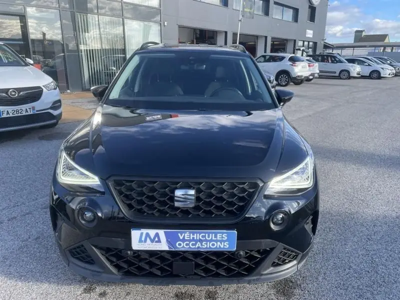 Vue de face d'un SEAT Arona noir 2023 avec calandre hexagonale et phares LED allumés sur parking extérieur.