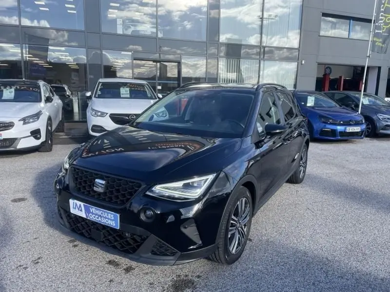Vue 3/4 avant droite d’un SEAT Arona noir 2023 avec calandre distinctive et jantes alliage, stationné devant un showroom.