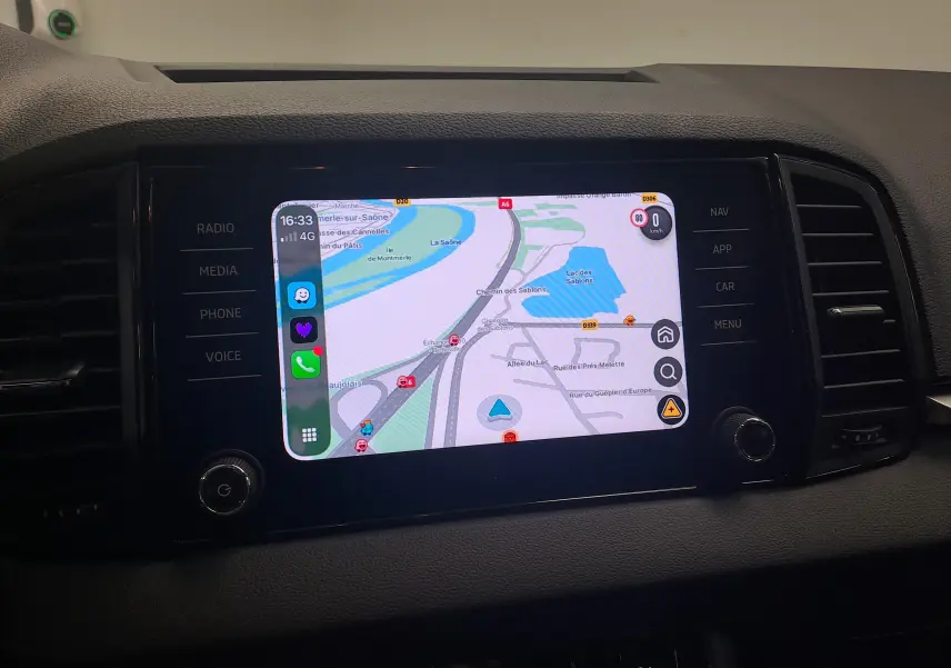 Écran central tactile du Skoda Karoq 2025 blanc lune, affichant une carte de navigation avec commandes latérales.