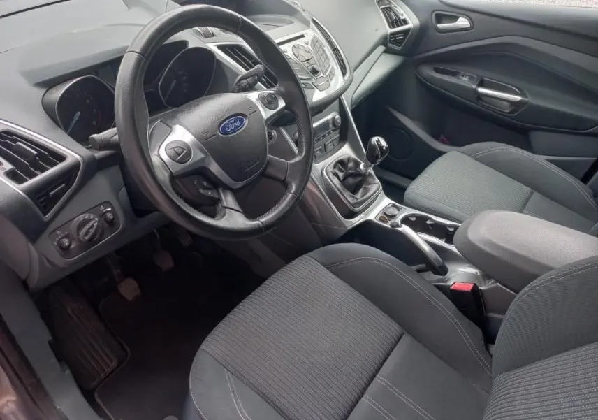 Vue intérieure côté conducteur du Ford C-MAX gris 2015, montrant le volant, la boîte manuelle et les sièges tissu noirs.