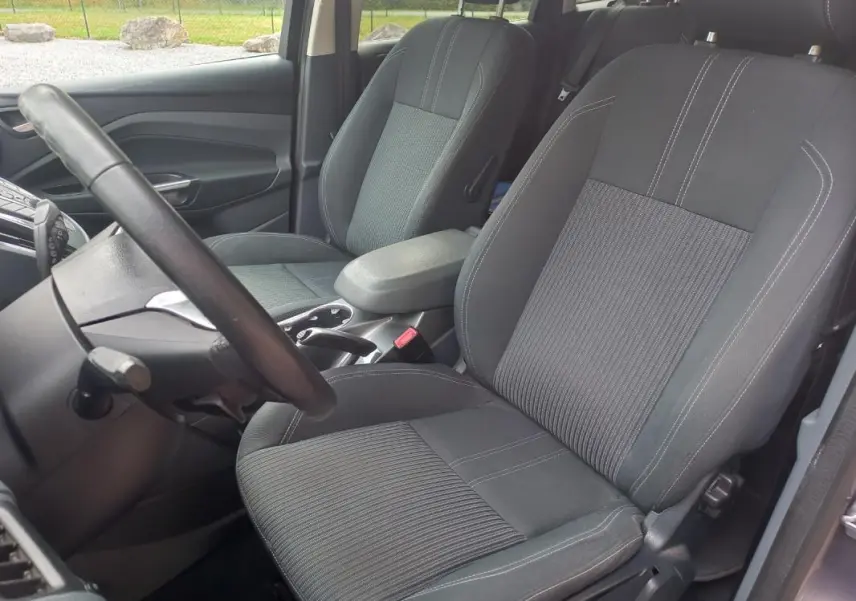 Vue intérieure côté conducteur du Ford C-MAX gris 2015, montrant les sièges avant en tissu avec coutures contrastées.