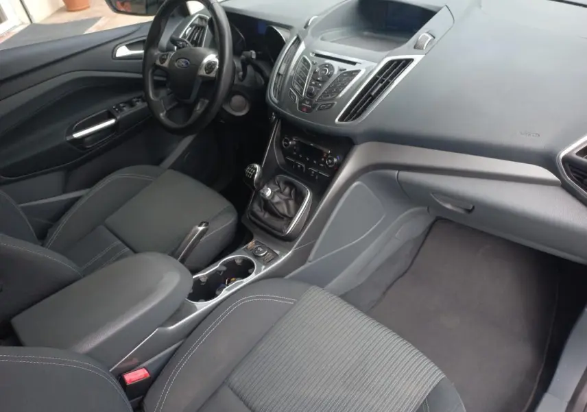 Vue intérieure côté conducteur du Ford C-MAX gris 2015, mettant en valeur le tableau de bord et la boîte manuelle.