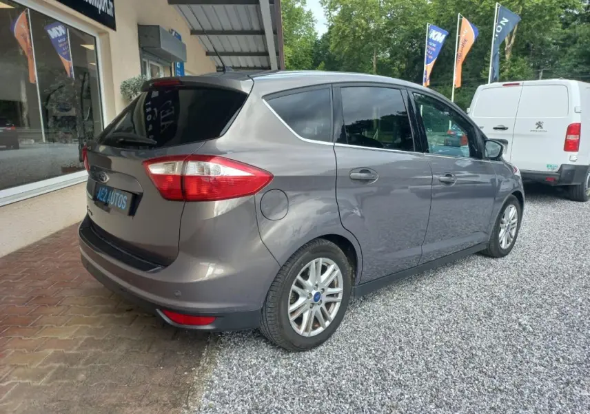 Ford C-MAX gris vue 3/4 arrière droit, avec vitres teintées et jantes alliage, stationné sur gravier.
