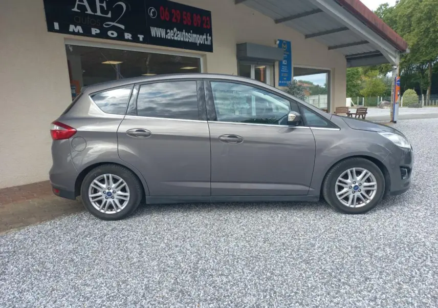 Vue de profil côté droit d'une Ford C-MAX gris métallisé de 2015, stationnée devant un bâtiment commercial.