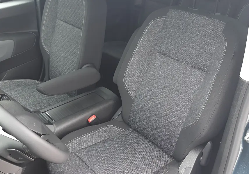 Vue intérieure côté conducteur du Peugeot Rifter bleu Kiama 2026, sièges tissu gris avec accoudoir central.