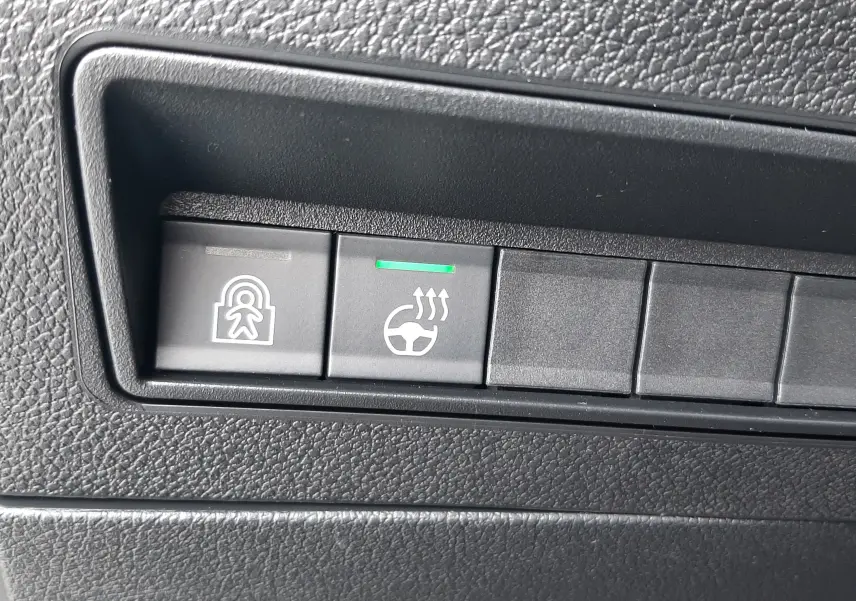 Boutons de commande du volant chauffant et de la sécurité enfants sur le tableau de bord noir du Peugeot Rifter bleu Kiama.