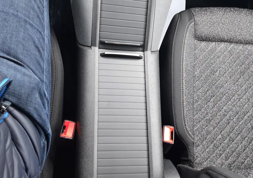 Vue plongeante sur la console centrale noire et les sièges tissu gris du Peugeot Rifter III Ph.2 intérieur.