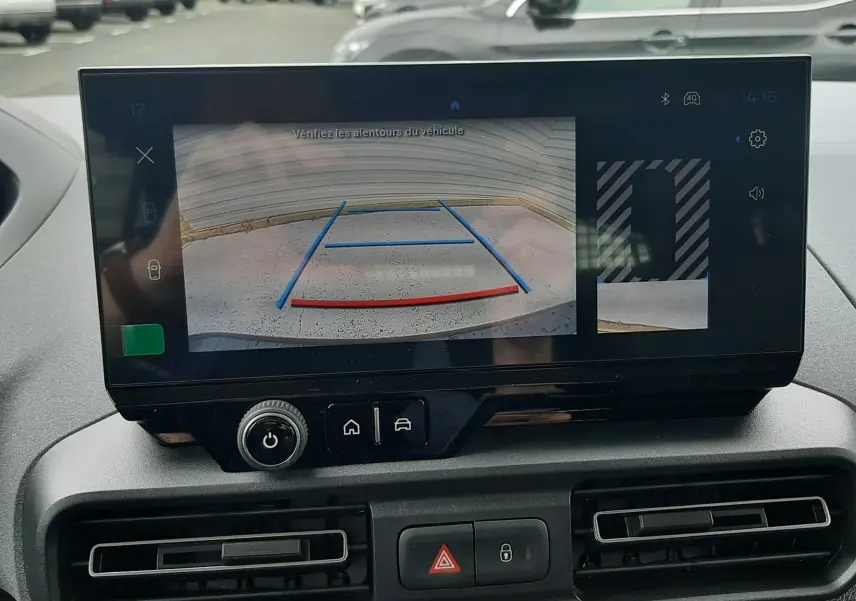 Vue intérieure centrée sur l'écran tactile affichant la caméra de recul du Peugeot Rifter bleu Kiama, avec tableau de bord et aérateurs visibles.